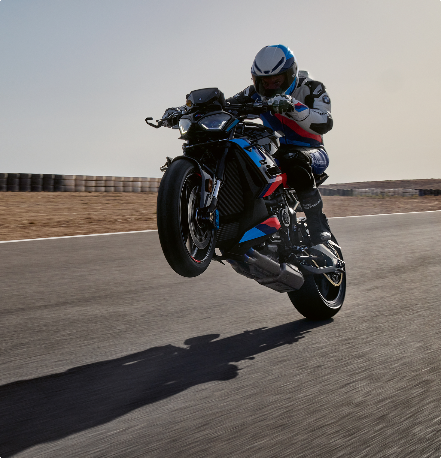 Action shot of a rider performing a wheelie on a blue and black BMW M 1000 R sport motorcycle on a paved trac