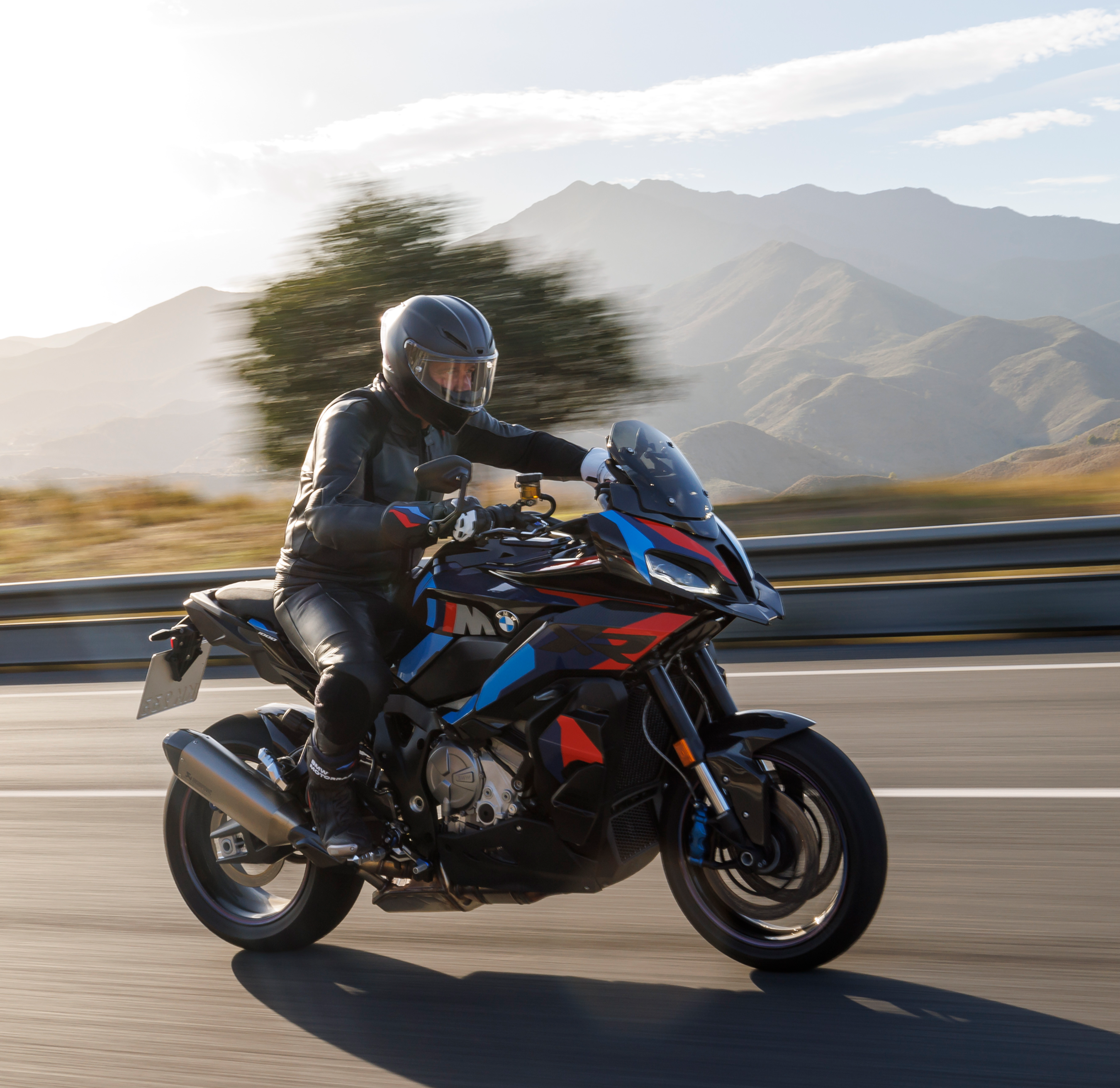 A rider on a BMW S 1000 XR sport-touring motorcycle traveling along a scenic mountain road, representing Marzocchi’s platform integration for road and adventure bikes