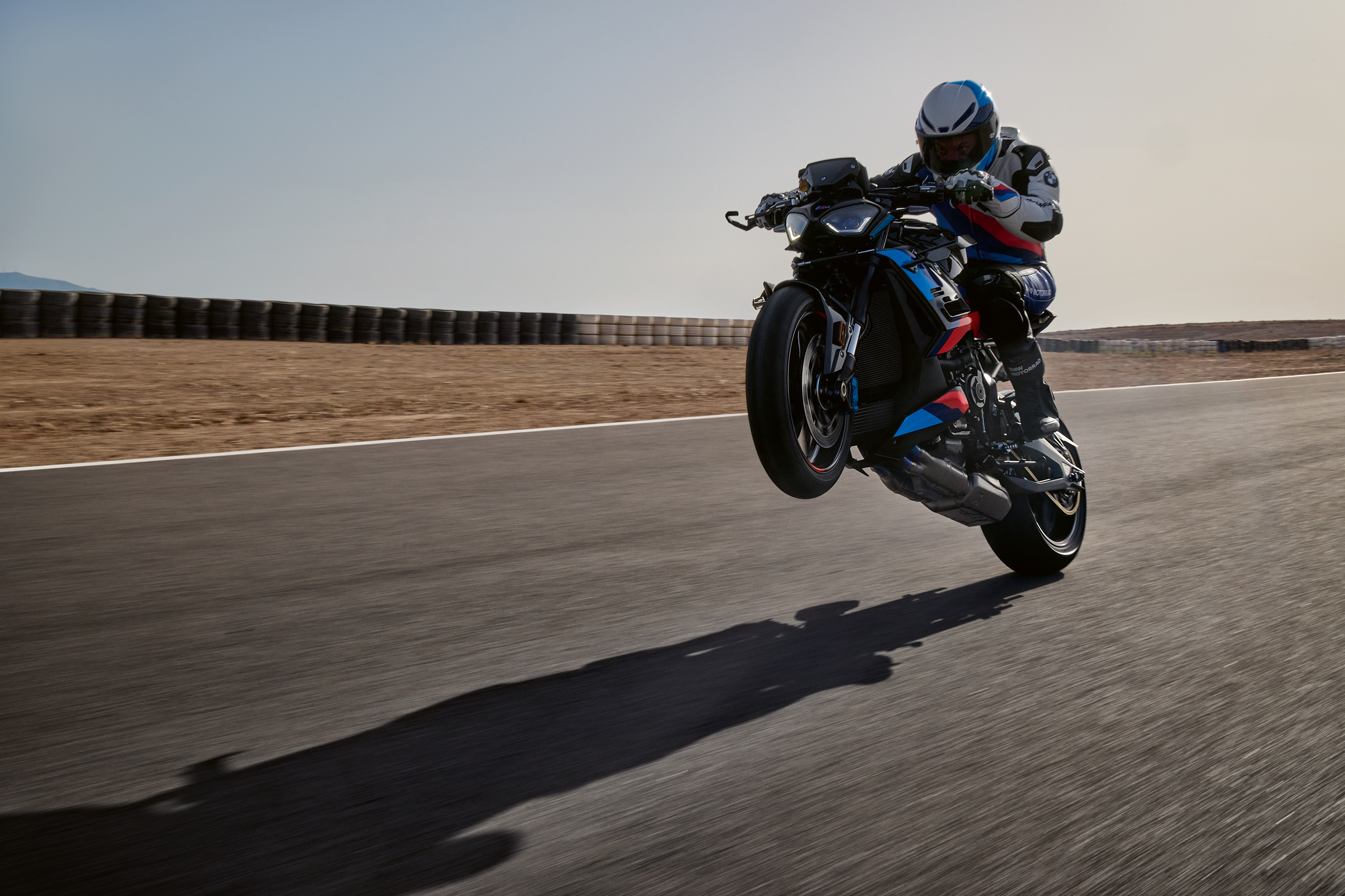 Action shot of a rider performing a wheelie on a BMW M 1000 R sport motorcycle on a paved track.
