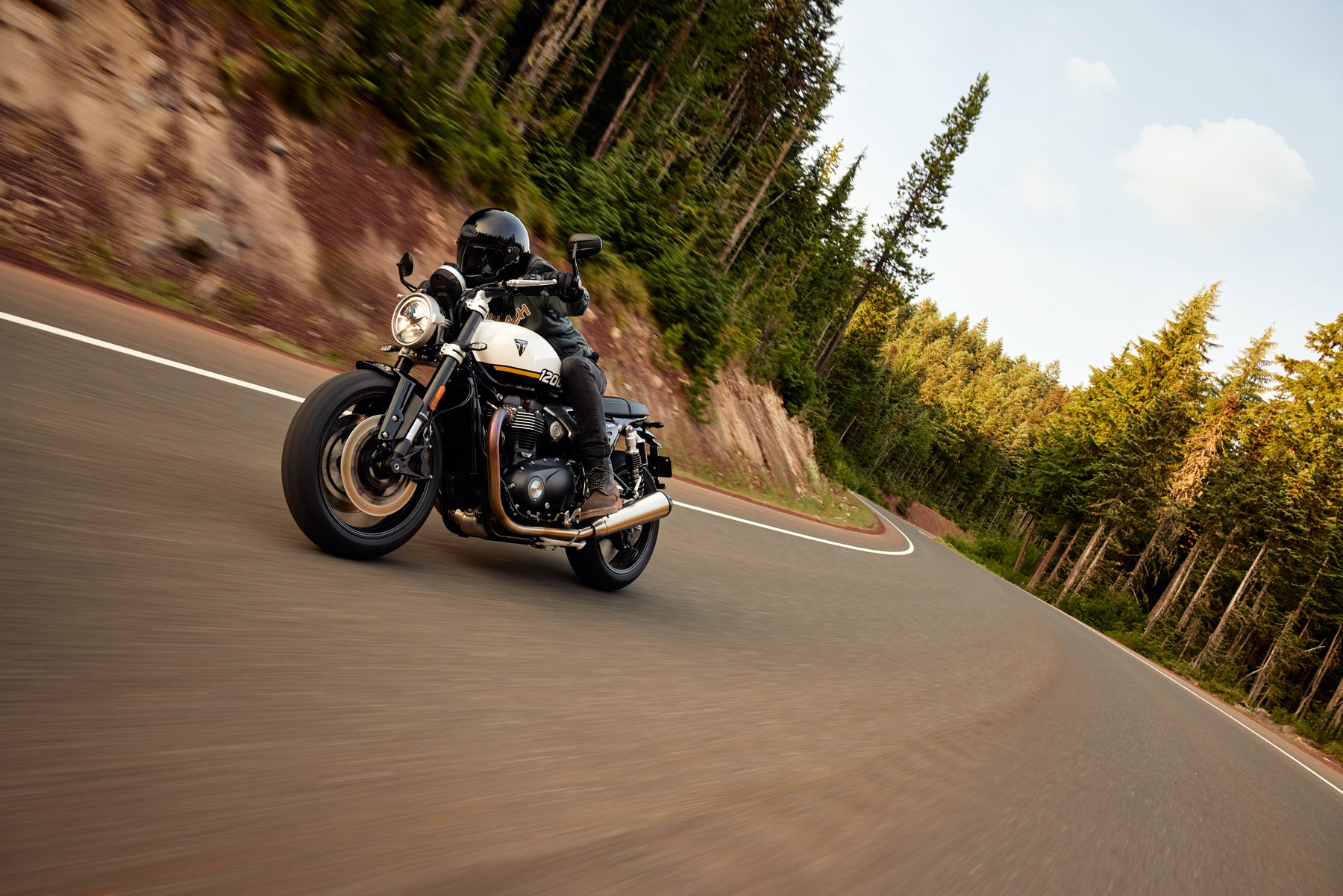 Rider leaning a Triumph Speed Twin 1200 through a winding forest road, showcasing classic modern styling and responsive road handling.