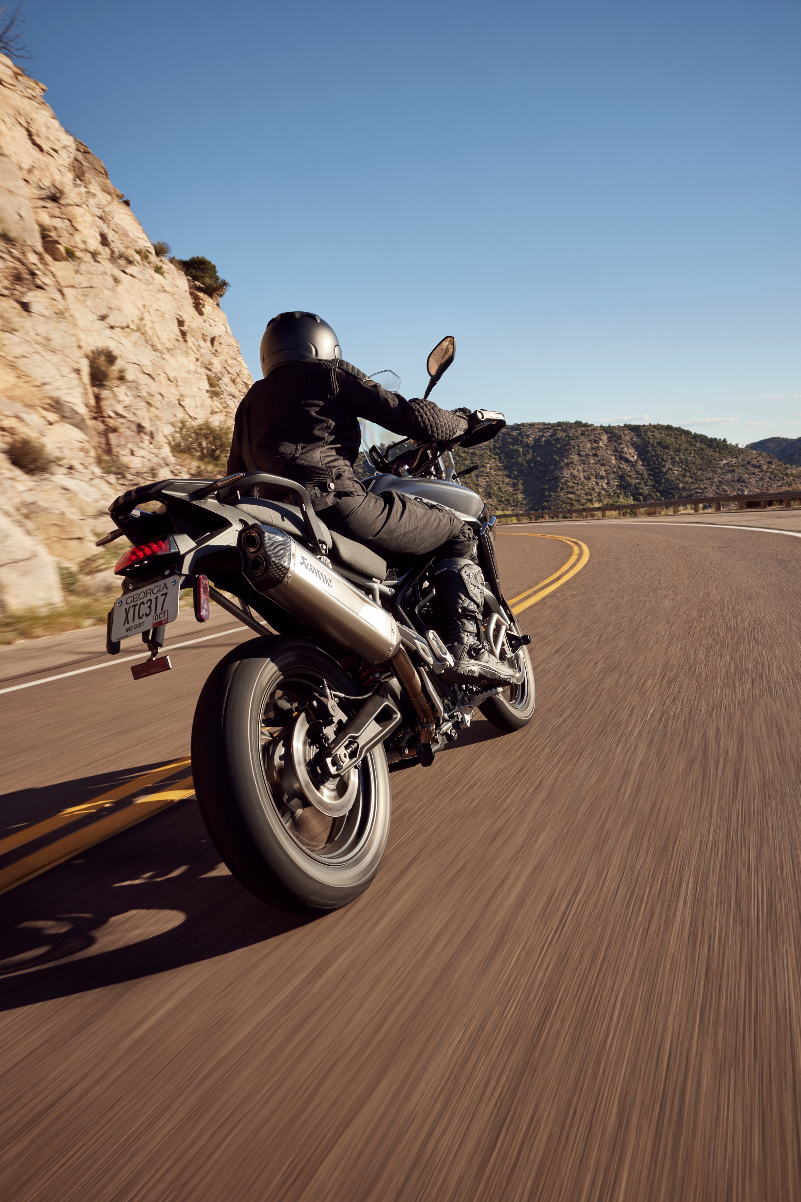 Triumph Tiger 900 GT Pro MY24 riding on winding mountain road in sunlight.