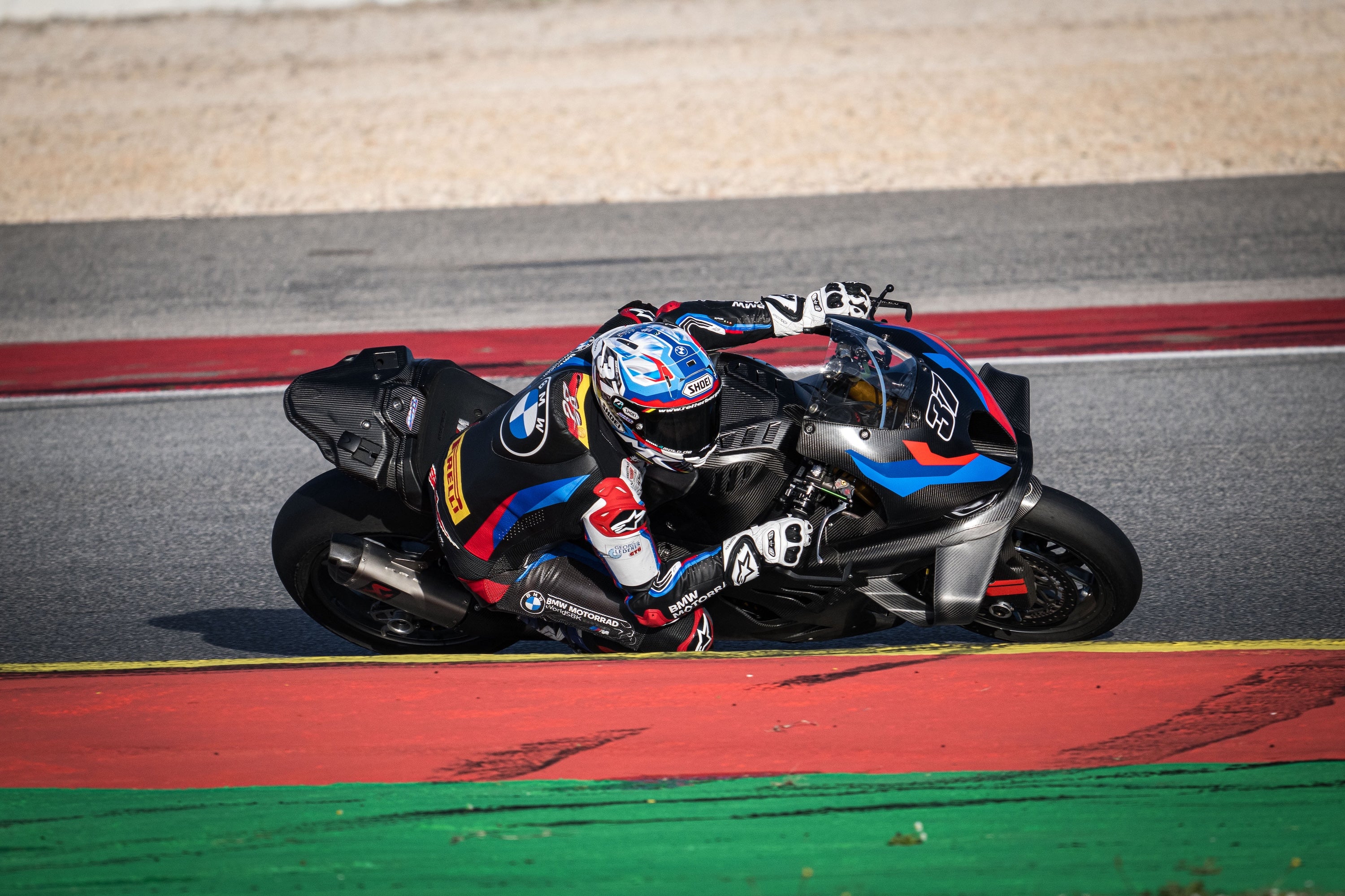 High-angle shot of a BMW M 1000 RR racing motorcycle leaning over a red and green curb on the Algarve International Circuit during professional track testing.