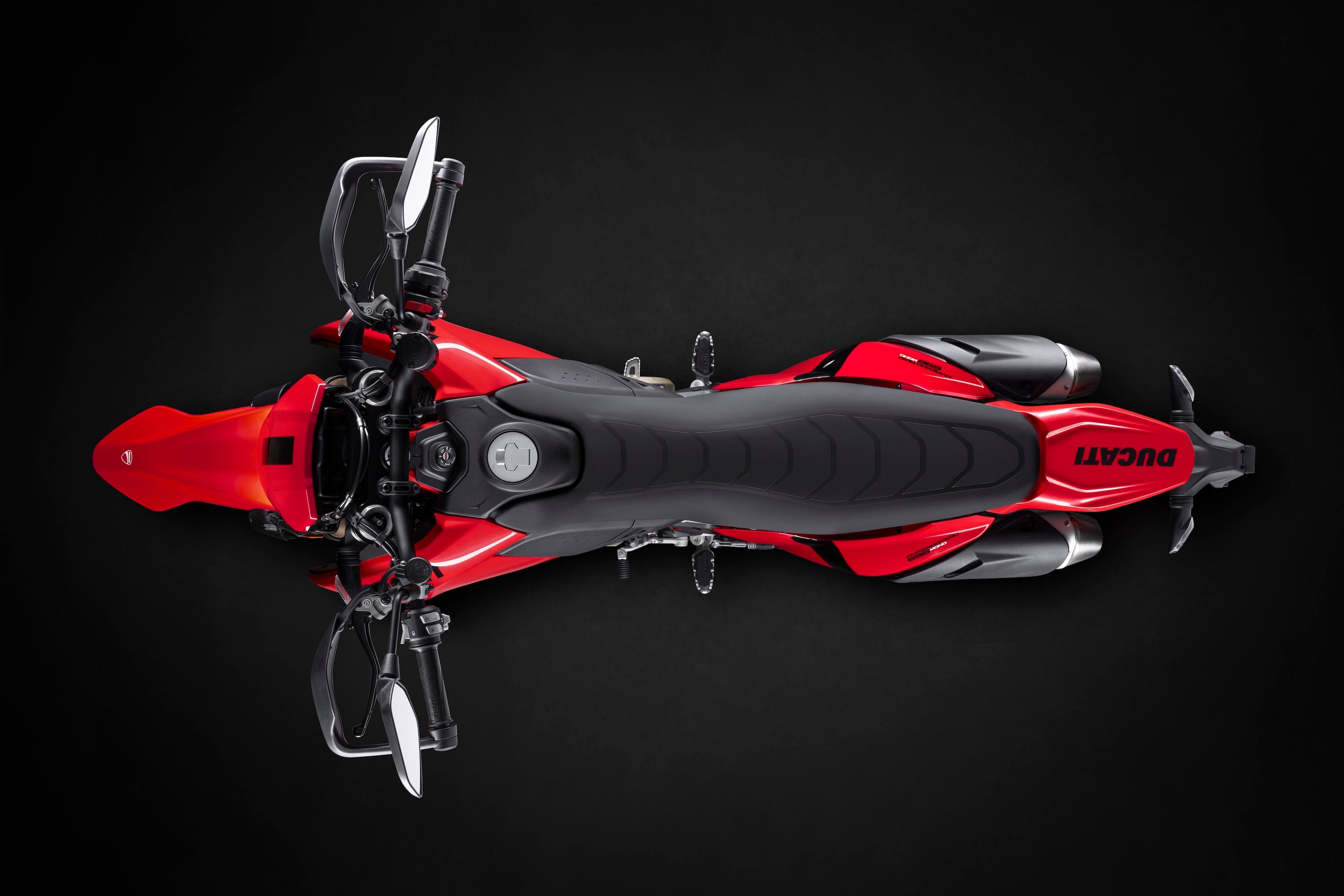 Top-down overhead view of a red Ducati Hypermotard 698 Mono, highlighting its slim seat design, fuel tank, and symmetrical dual exhaust pipes.