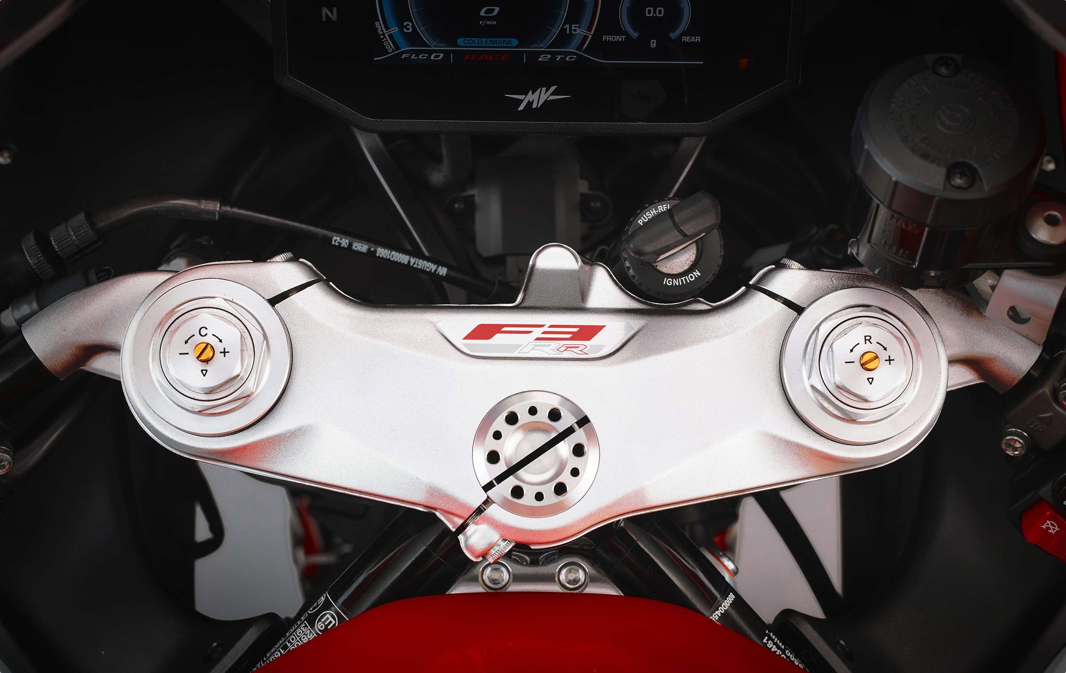 Motorcycle top triple clamp with front fork compression and rebound adjusters for performance suspension tuning.