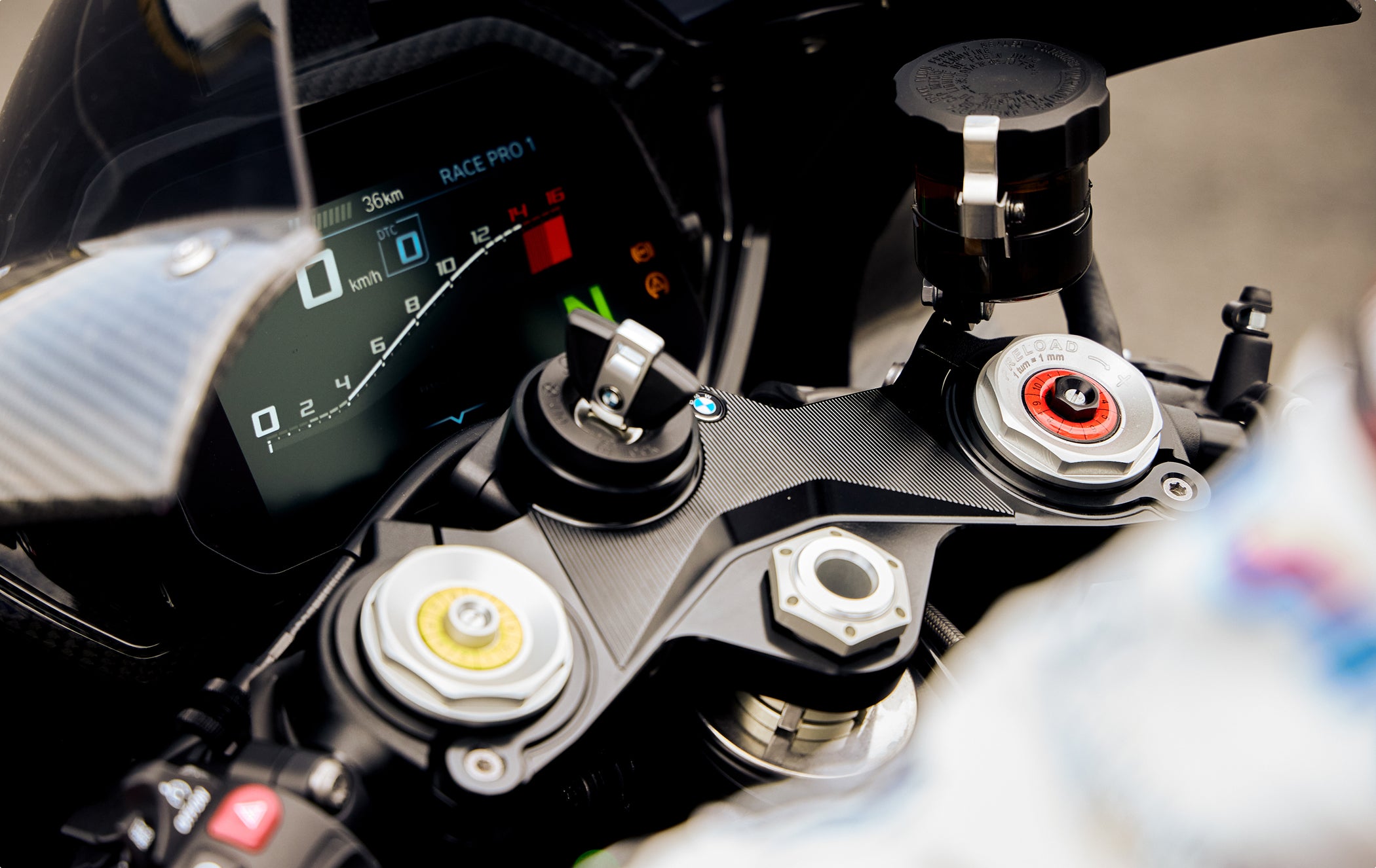 Close-up of motorcycle front suspension triple clamp with adjustable preload and damping controls.