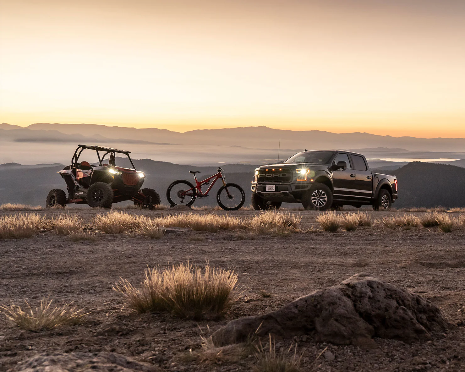 Off-road adventure lineup at dawn: Marzocchi-equipped mountain bike, side-by-side, and performance truck group shot in a desert mountain landscape.