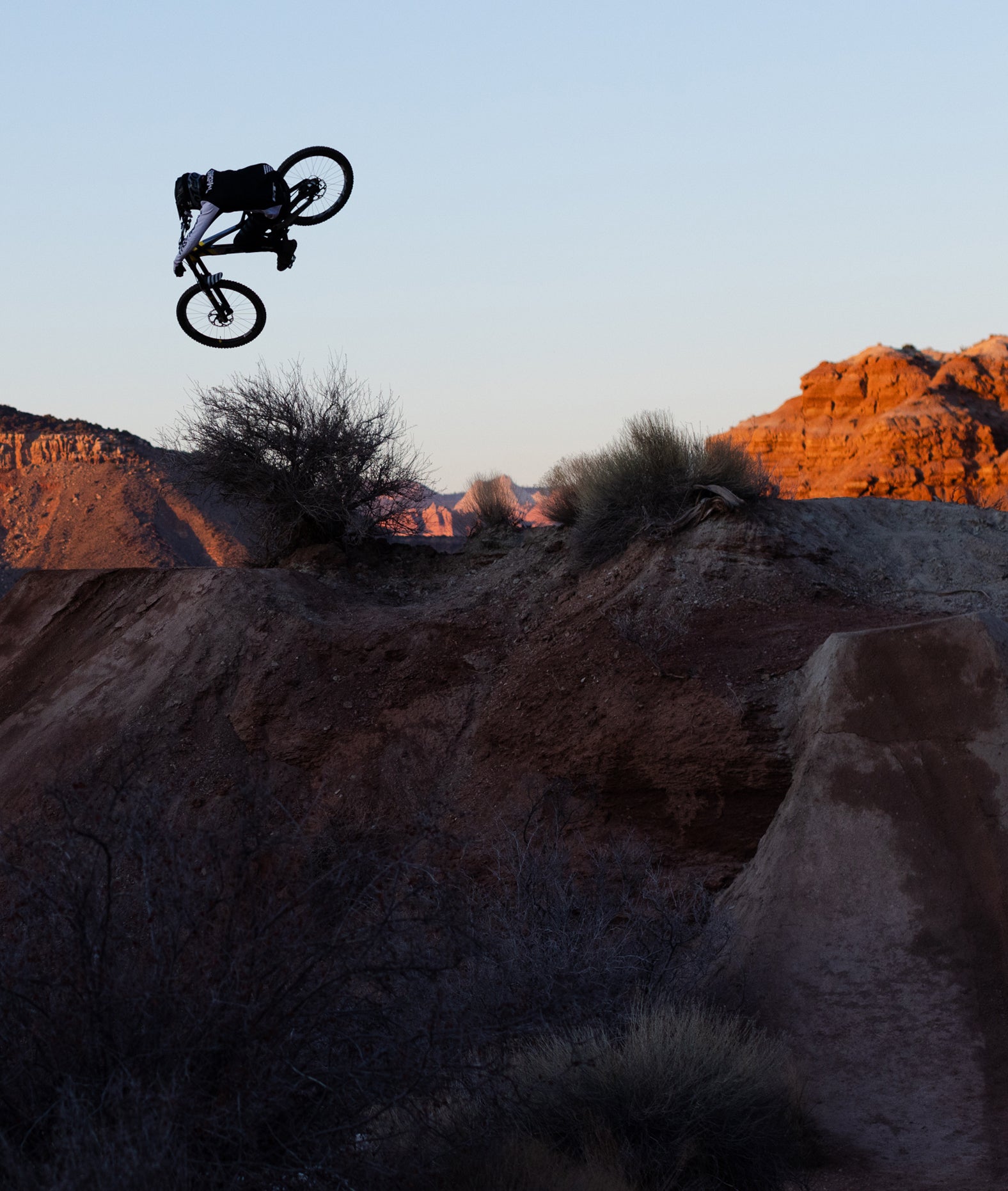 Person on a bicycle performing a jump in a desert landscape with rocky formations.