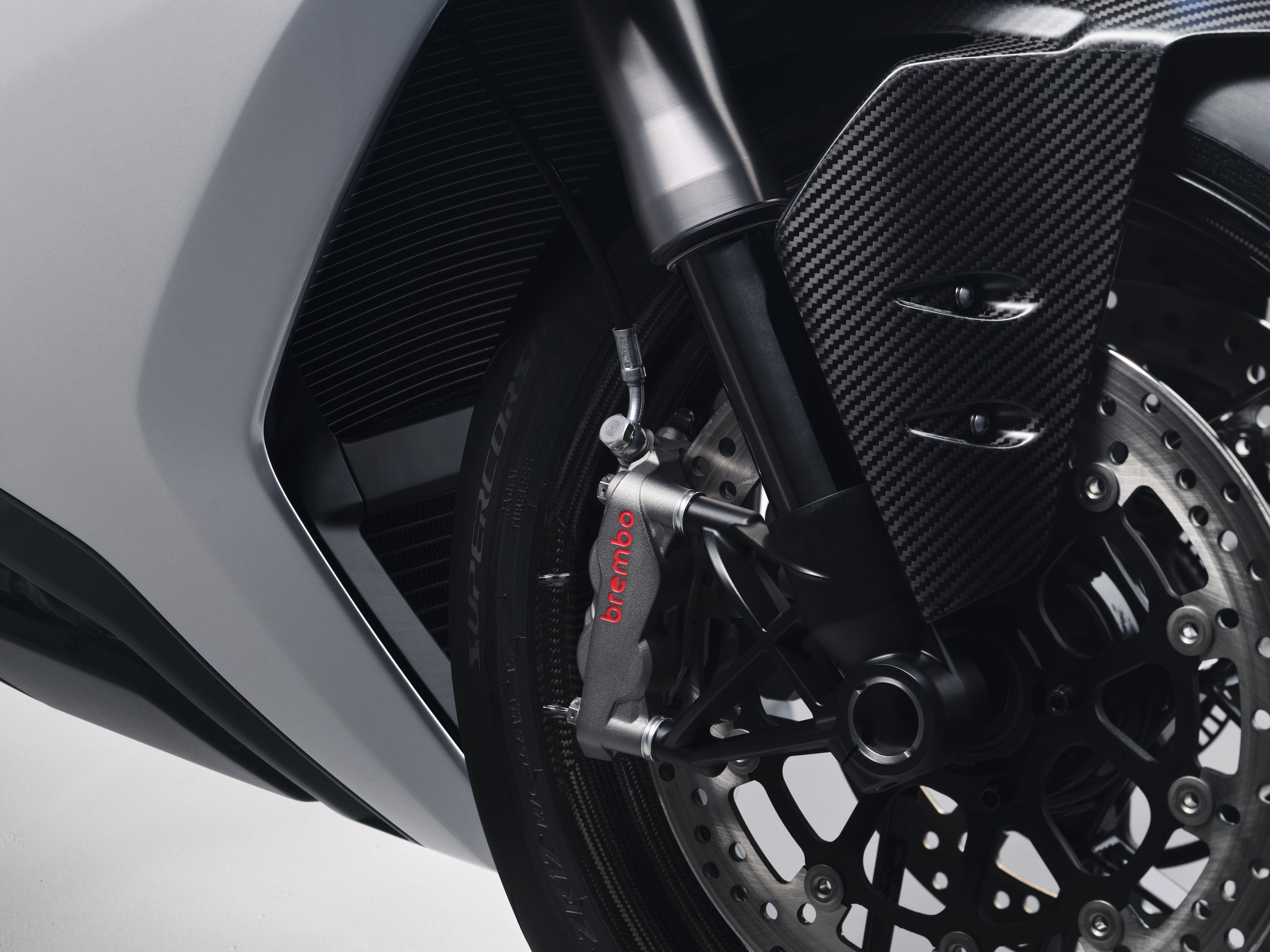 Close-up of the Norton Manx R front wheel assembly, featuring a Brembo radial brake caliper, carbon fiber fender, and Pirelli Supercorsa tire.