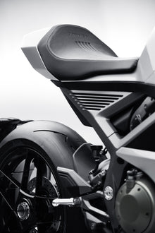 A close-up of a silver motorcycle's rear seat and tire, showing fine stitching on the black leather and the word Norton pressed into the material.