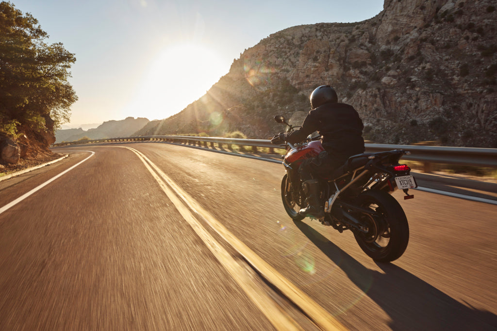 Motorcyclist riding a red sport bike on a winding mountain road at sunset.